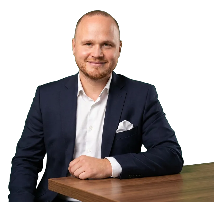 Patrick Steeger im dunklen Sakko sitzt an einem Holztisch und blickt lächelnd in die Kamera